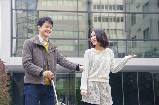 写真　白杖を持っている人を手引きしている様子