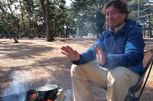 （写真）焚火の前に座る片山さんの様子