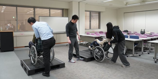 （写真）車いす実技研修の中で、車いすでの段差の乗り降りのサポートを体験している様子