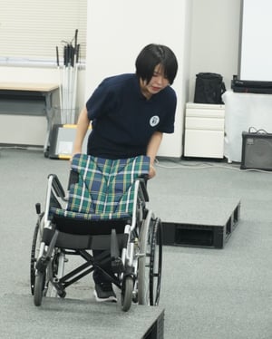 （写真）車いす実技研修で、講師が段差の上り下りのサポート方法をお伝えしている様子