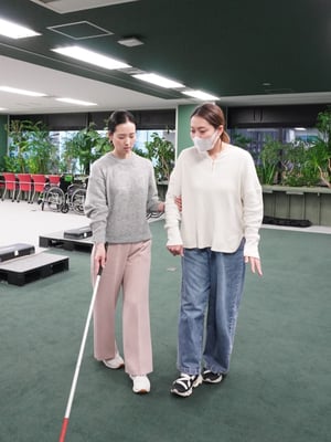 （写真）堀さんが視覚障害の実技研修の中で、目を閉じた状態で誘導される体験をしている様子