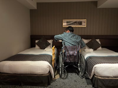 （写真）客室のベッドの間を車いすで通れるか確認している様子