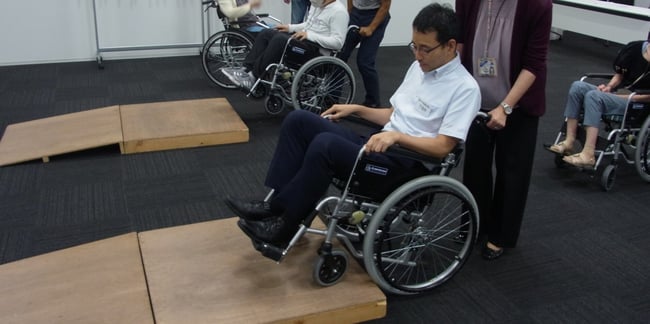 （写真）受講者が車いす実技研修で段差の上り下りのサポートを行っている様子