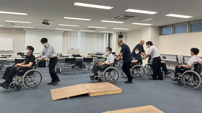 （写真）視覚障害者体験で当事者役の方をイスまで誘導をしている様子