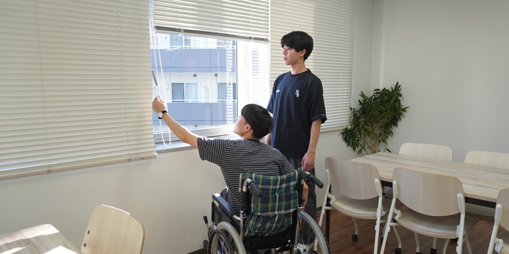 （写真）車いすの実技研修で、車いすに乗った方と一緒に窓を開けている様子